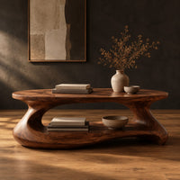Coffee table with a sculpted pebble base and low shelf in a dark studio against a charcoal plaster wall