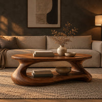 Coffee table with a sculpted pebble base and low shelf in a dark living room at golden hour