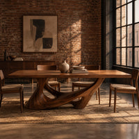 Dining table with a slab top on a sculpted pedestal with open cutouts in an industrial loft dining room with exposed brick