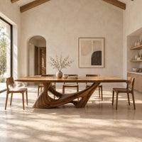 Dining table with a slab top on a sculpted pedestal with open cutouts in a bright open plan dining room