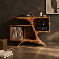 Corner detail of sculpted wood record console with swooping legs and open bays beside wood, brass and linen samples