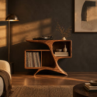 Sculpted wood record console with swooping legs and open bays in a dark living room at golden hour