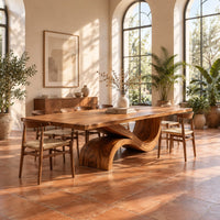 Dining table with a long plank top and one sweeping ribbon base in a bright dining room with arched windows and plants