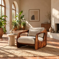 Chair with thick sculpted wooden side panels, oval cutouts and a cushioned seat in a bright living room with arched windows and plants