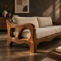 Corner detail of sculpted wood sofa with open loop arms and a wavy lower rail beside wood, brass and linen samples