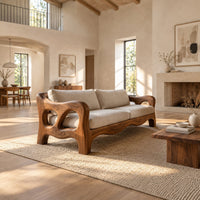 Sculpted wood sofa with open loop arms and a wavy lower rail in a bright open plan living room