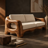 Corner detail of sofa with thick sculpted arms that have oval openings and a wavy base edge beside wood, brass and linen samples