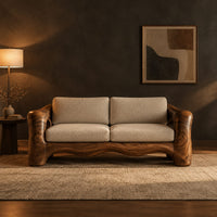 Sofa with thick sculpted arms that have oval openings and a wavy base edge in a dark living room at golden hour