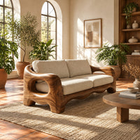 Sofa with thick sculpted arms that have oval openings and a wavy base edge in a bright living room with arched windows and plants