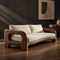 Solid wood sofa with sculpted open loop arms and a long cream seat cushion, three-quarter view showing the grain