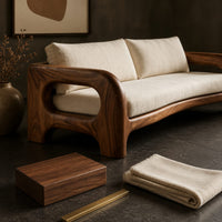 Corner detail of solid wood sofa with sculpted open loop arms and a long cream seat cushion beside wood, brass and linen samples