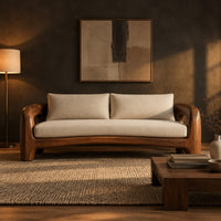 Solid wood sofa with sculpted open loop arms and a long cream seat cushion in a dark living room at golden hour