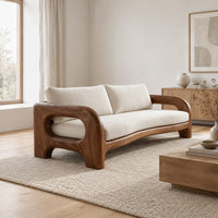 Solid wood sofa with sculpted open loop arms and a long cream seat cushion in a Scandinavian living room with white walls