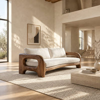 Solid wood sofa with sculpted open loop arms and a long cream seat cushion in a bright open plan living room
