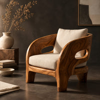 Corner detail of sculpted wooden lounge chair with oval side cutouts and cream cushions beside wood, brass and linen samples