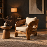 Sculpted wooden lounge chair with oval side cutouts and cream cushions in a dark living room at golden hour