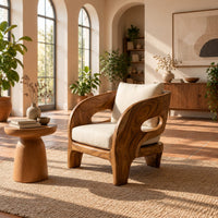Sculpted wooden lounge chair with oval side cutouts and cream cushions in a bright living room with arched windows and plants