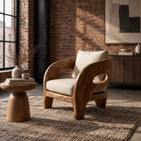 Sculpted wooden lounge chair with oval side cutouts and cream cushions in an industrial loft living room with exposed brick