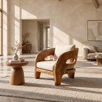 Sculpted wooden lounge chair with oval side cutouts and cream cushions in a bright open plan living room
