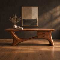 Long desk with sculpted swooping legs and a two drawer unit under the top in a dark studio against a charcoal plaster wall