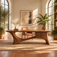 Long desk with sculpted swooping legs and a two drawer unit under the top in a bright home office with arched windows and plants