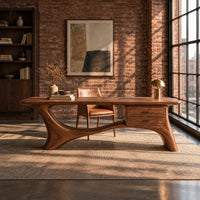 Long desk with sculpted swooping legs and a two drawer unit under the top in an industrial loft home office with exposed brick