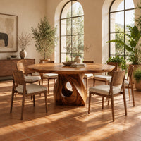 Dining table with a twisted pedestal base and a softly waved edge top in a bright dining room with arched windows and plants