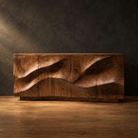 Low sideboard with wave relief across four panels and a recessed plinth base in a dark studio against a charcoal plaster wall