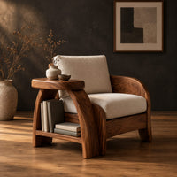 Sculpted wood chair with an oval arm ledge and a cream seat cushion in a dark studio against a charcoal plaster wall