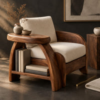 Corner detail of sculpted wood chair with an oval arm ledge and a cream seat cushion beside wood, brass and linen samples