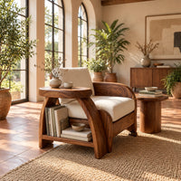 Sculpted wood chair with an oval arm ledge and a cream seat cushion in a bright living room with arched windows and plants