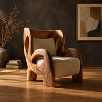 Sculpted lounge chair with looping carved arms, cutout back and cream cushions in a dark studio against a charcoal plaster wall