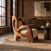 Sculpted lounge chair with looping carved arms, cutout back and cream cushions in an industrial loft living room with exposed brick