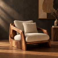 Lounge chair with a sculpted wood shell and thick cream cushions in a dark studio against a charcoal plaster wall