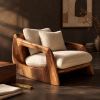 Corner detail of lounge chair with a sculpted wood shell and thick cream cushions beside wood, brass and linen samples