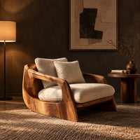 Lounge chair with a sculpted wood shell and thick cream cushions in a dark living room at golden hour