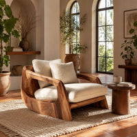 Lounge chair with a sculpted wood shell and thick cream cushions in a bright living room with arched windows and plants
