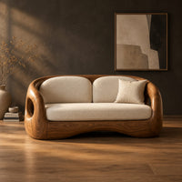 Carved wood shell sofa with oval arm openings and a cushioned seat in a dark studio against a charcoal plaster wall