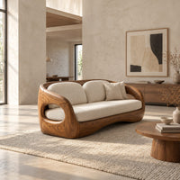 Carved wood shell sofa with oval arm openings and a cushioned seat in a bright open plan living room