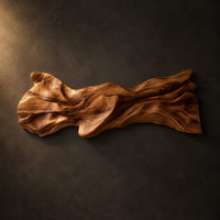 Long sculpted wood wall art with layered flowing folds and an uneven outline on a dark charcoal plaster wall