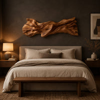 Long sculpted wood wall art with layered flowing folds and an uneven outline above a bed in a dusk lit bedroom