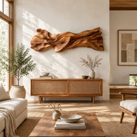 Long sculpted wood wall art with layered flowing folds and an uneven outline in a bright sunroom with green plants