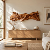 Long sculpted wood wall art with layered flowing folds and an uneven outline above a light oak sideboard in daylight