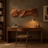 Long sculpted wood wall art with layered flowing folds and an uneven outline above a desk in a dark study corner