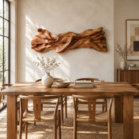 Long sculpted wood wall art with layered flowing folds and an uneven outline beside a dining table in natural light
