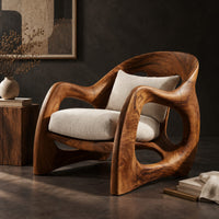 Corner detail of sculptural wooden chair with looping arms and teardrop side openings beside wood, brass and linen samples
