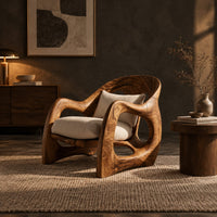 Sculptural wooden chair with looping arms and teardrop side openings in a dark living room at golden hour
