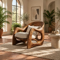 Sculptural wooden chair with looping arms and teardrop side openings in a bright living room with arched windows and plants