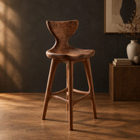 Bar stool with a winged backrest and a dished saddle seat in a dark studio against a charcoal plaster wall