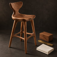 Corner detail of bar stool with a winged backrest and a dished saddle seat beside wood, brass and linen samples